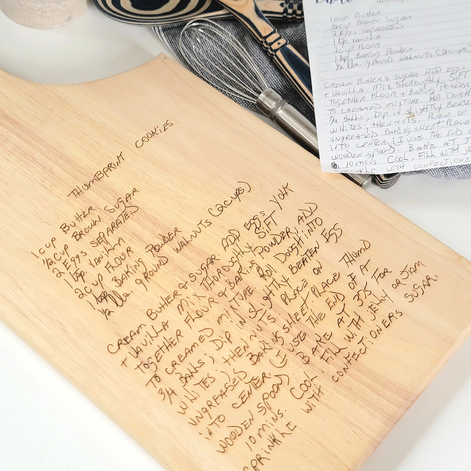 Handwritten thumbprint cookies recipe on wooden cutting board